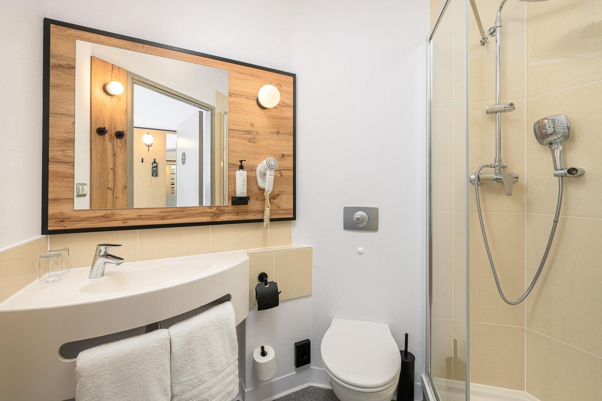 Un baño moderno con tocador de madera, un espejo grande, ducha con cabezal de mano y un inodoro.