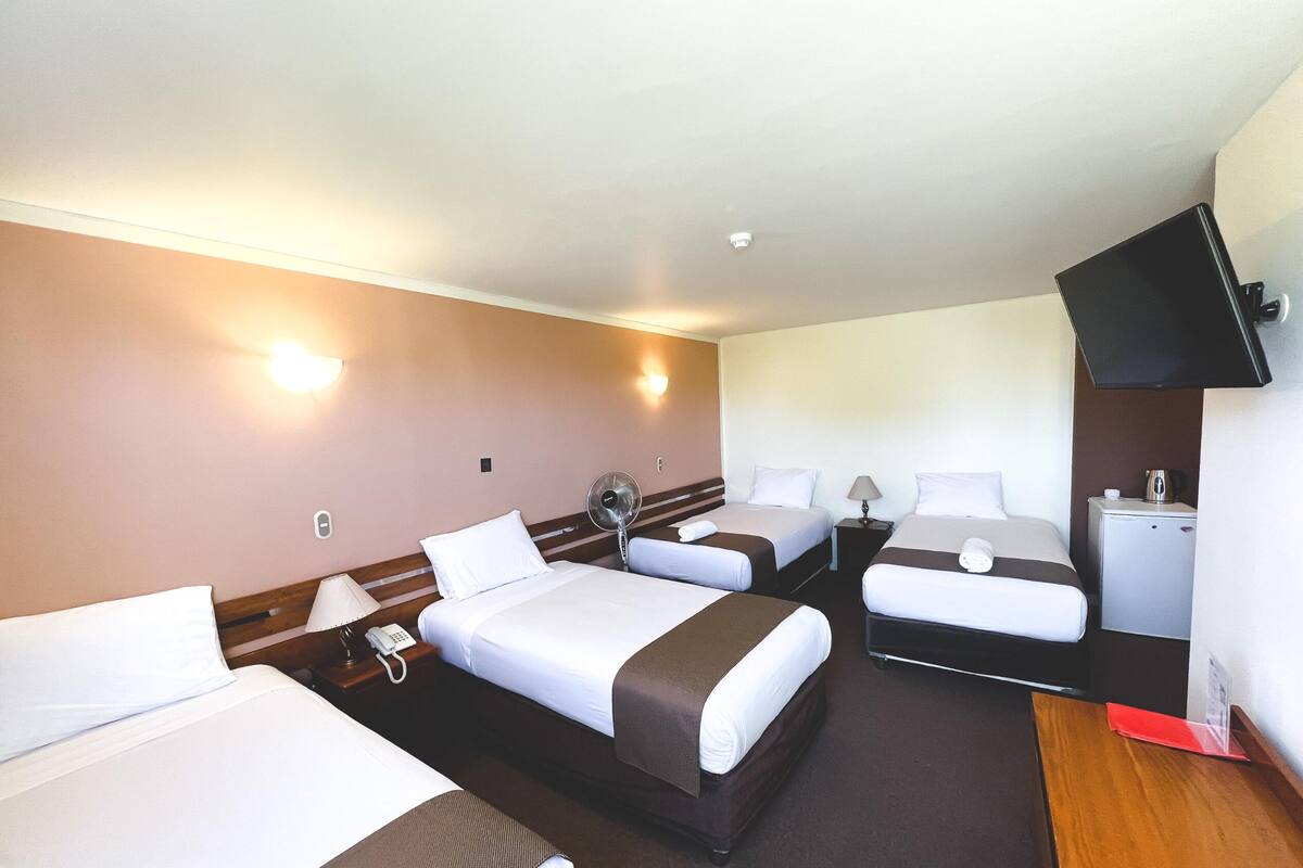 A hotel room with three beds, a TV, a desk, and a small kitchenette.