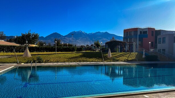 A swimming pool with clear blue water, surrounded by well-maintained lawns and a mountain range in the background. - DM Hoteles Arequipa (Arequipa)