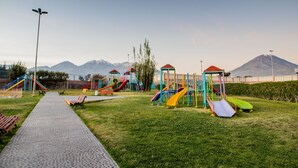 A playground with slides and climbing structures, a paved walkway, and a mountain in the background. - DM Hoteles Arequipa (Arequipa)