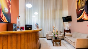 A reception area with a wooden counter, two sofas, a coffee table, and a TV on a stand. - DM Hoteles Arequipa (Arequipa)