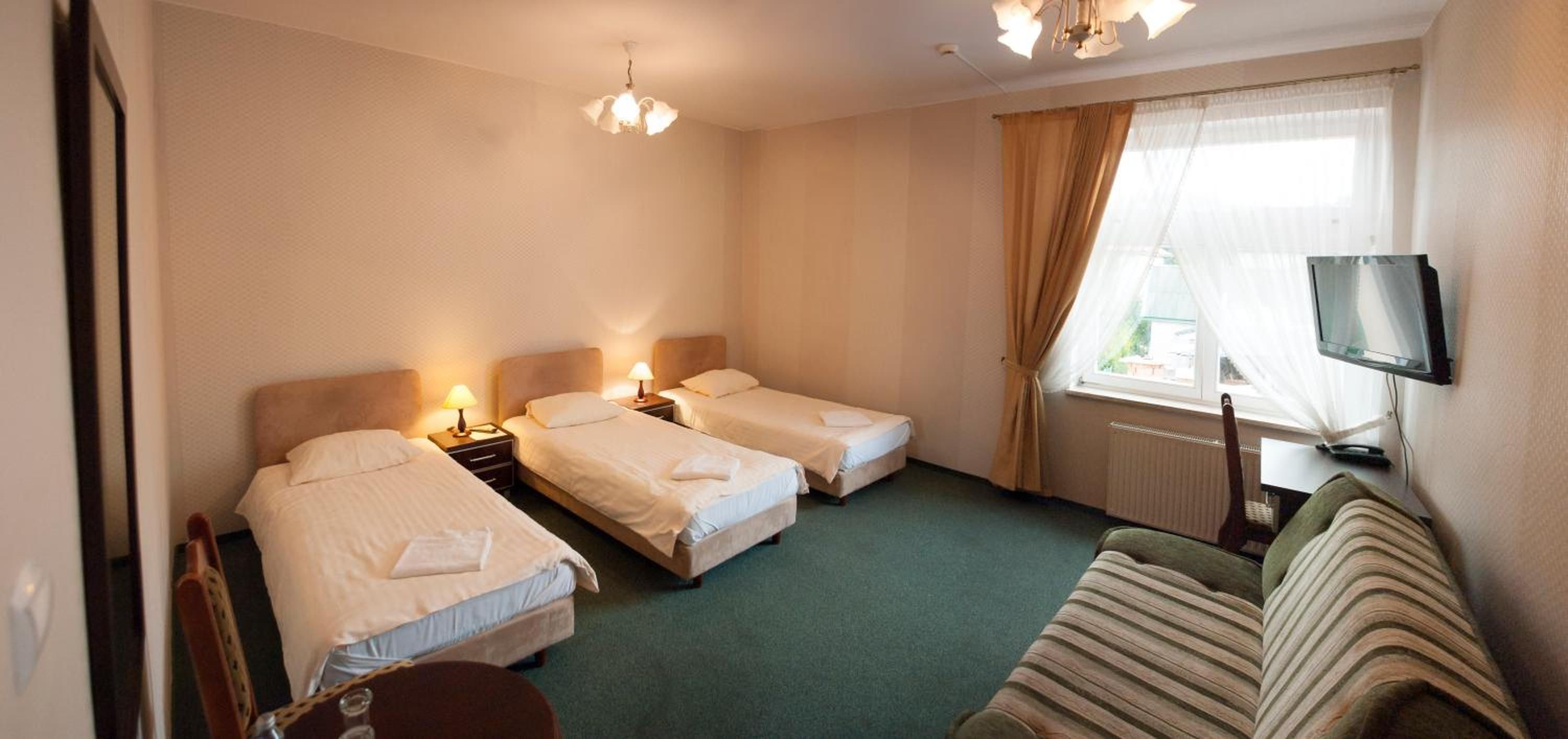 Une chambre d’hôtel avec deux lits simples, un canapé, une télévision et une fenêtre avec des rideaux.
