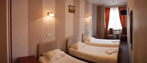A hotel room with two beds, a small table, a chair, a television, and a window with curtains.