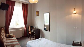 A hotel room with a bed, a desk, a chair, a TV, and a window with curtains.