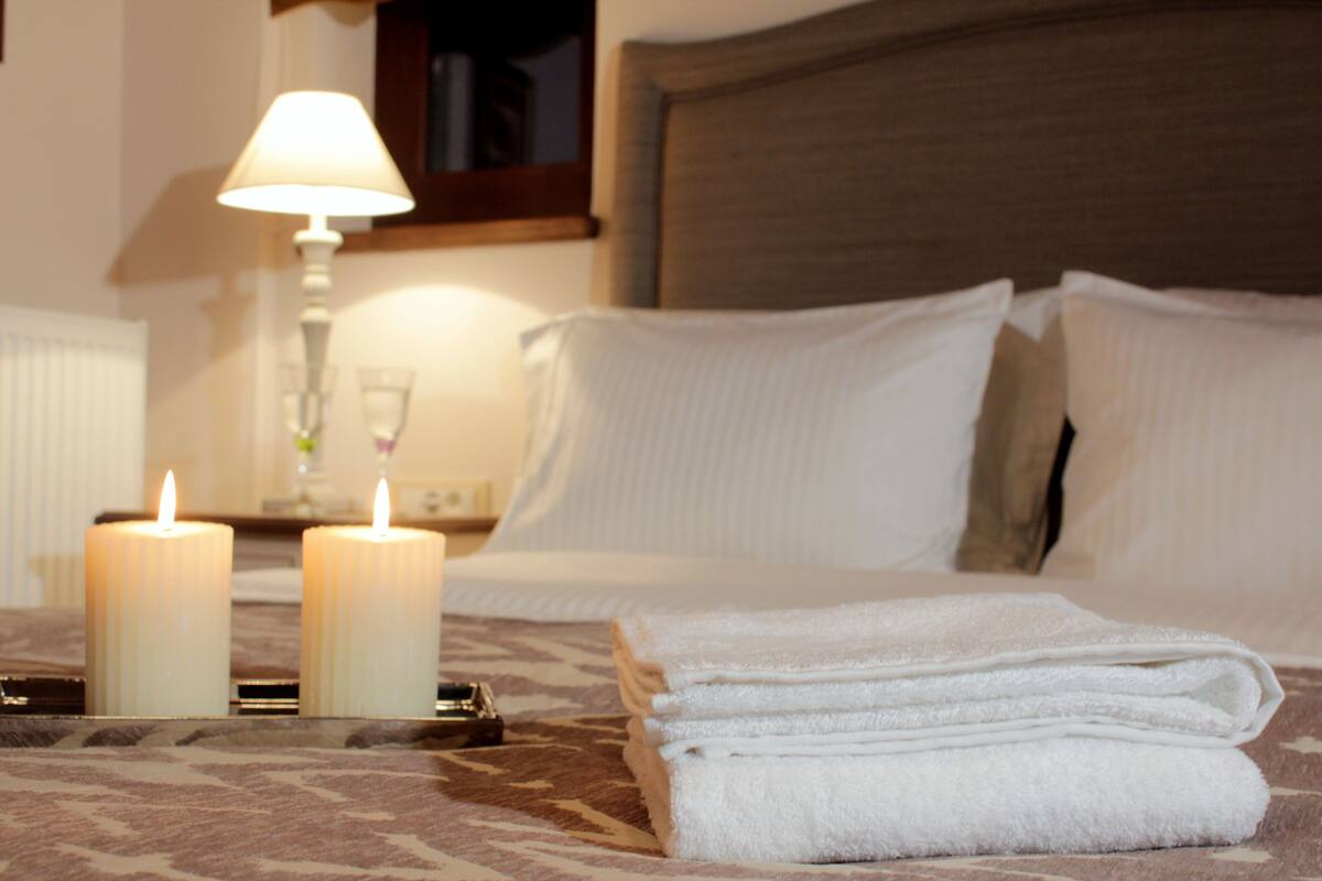 Un lit bien fait, avec du linge de lit blanc, deux bougies allumées et une table de chevet avec une lampe.