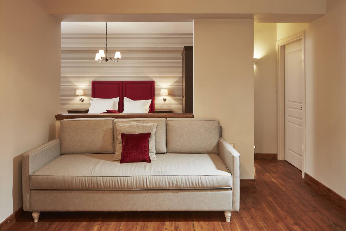 Une chambre d’hôtel moderne avec un canapé beige, une tête de lit rouge et un plancher en bois.