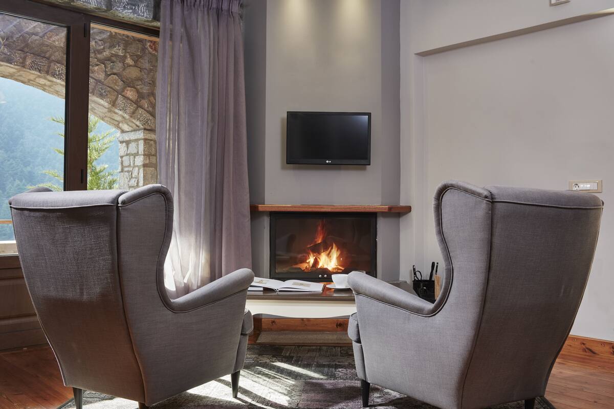Une pièce chaleureuse avec une cheminée, deux fauteuils, un téléviseur à écran plat et un mur en pierre.