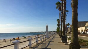 Un paseo marítimo con playa, palmeras y una estructura de columnas blancas.