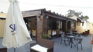 Un patio al aire libre con mobiliario de mimbre, una sombrilla blanca y un restaurante con puertas de vidrio.