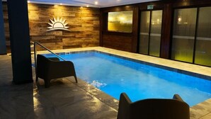 Una piscina interior con una pared de madera y un emblema de sol, una puerta de cristal y una silla junto a la piscina.