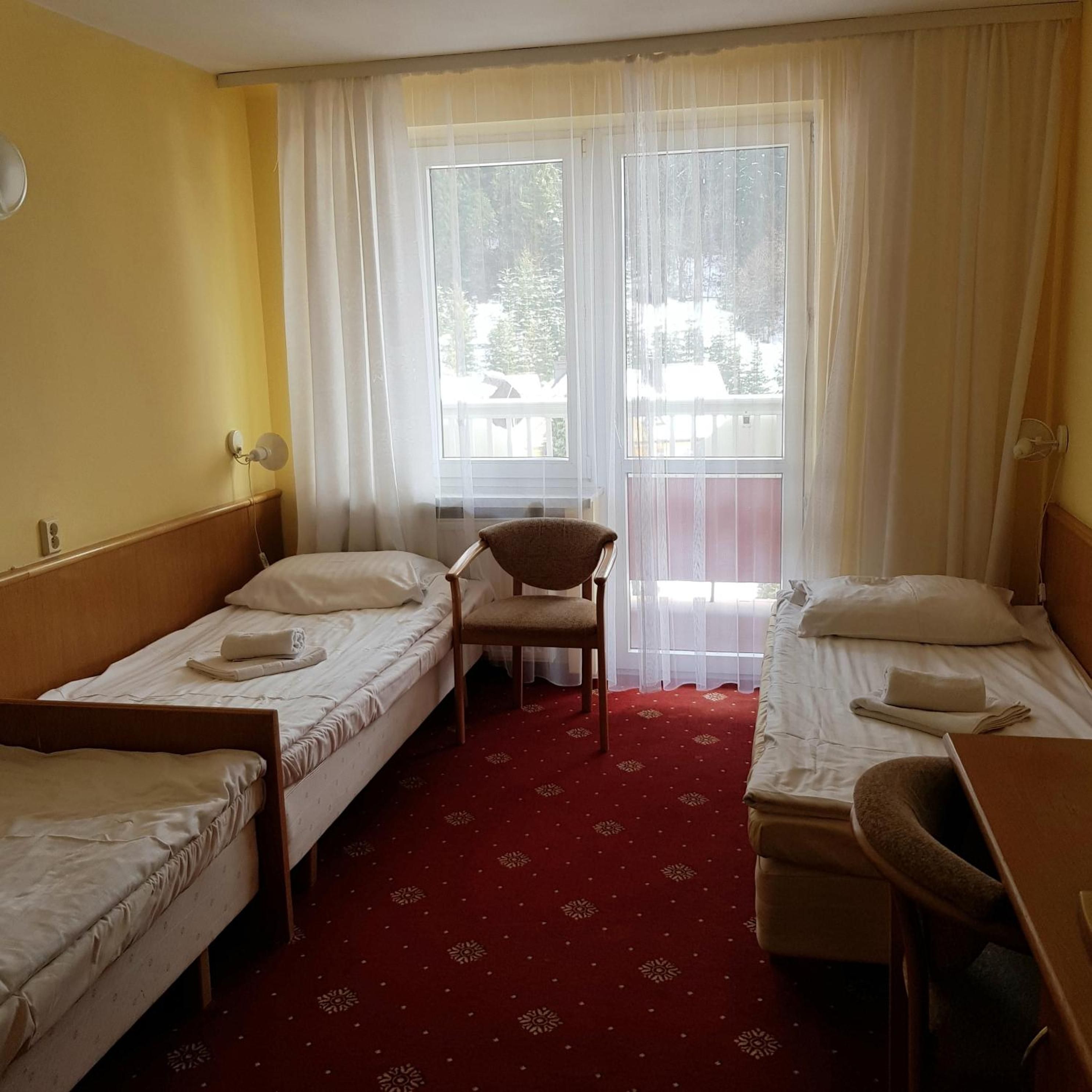 A hotel room with two single beds, a chair, a desk, and a window with curtains.