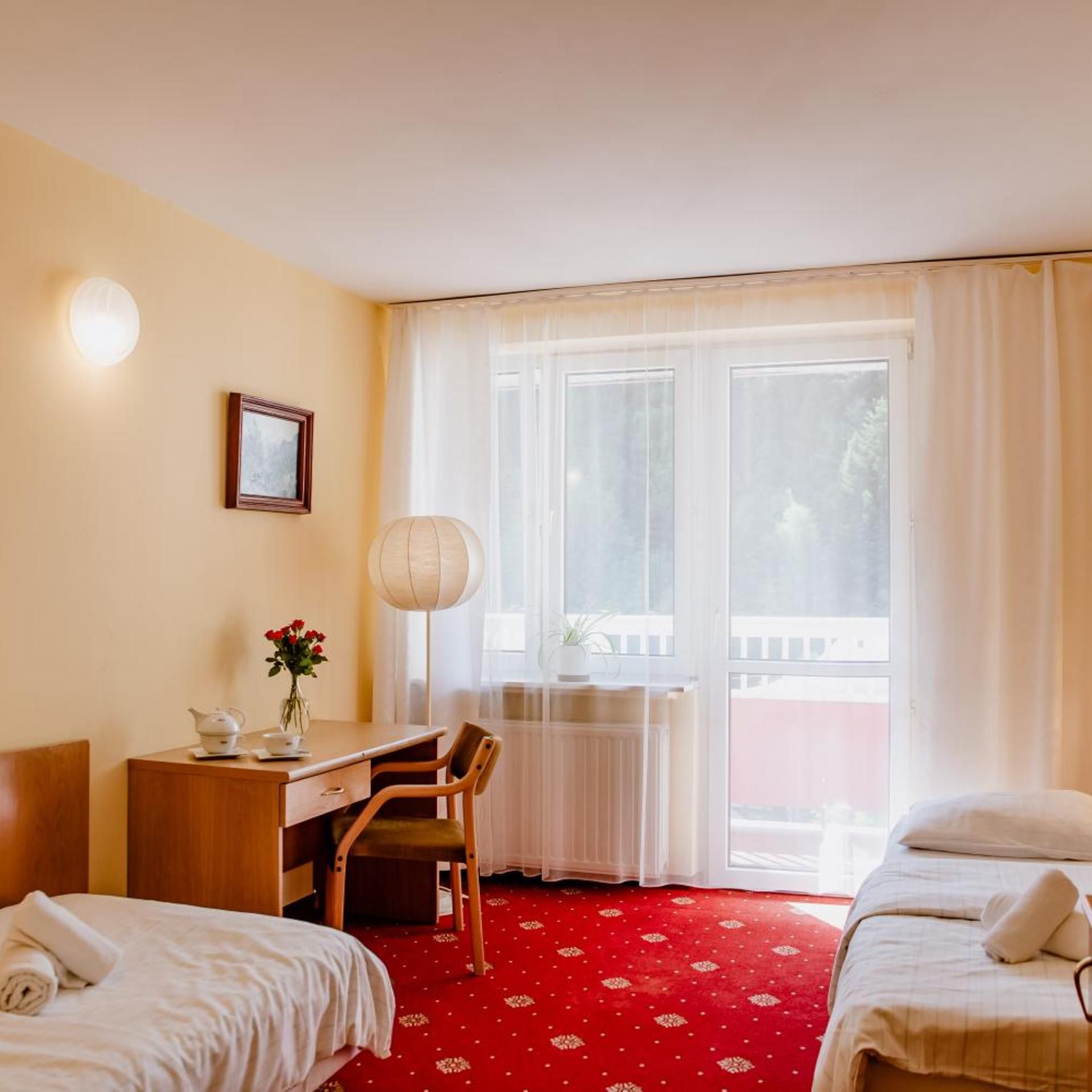 Una habitación de hotel con una cama, un escritorio con silla, una lámpara, una ventana con cortinas y vistas al exterior.