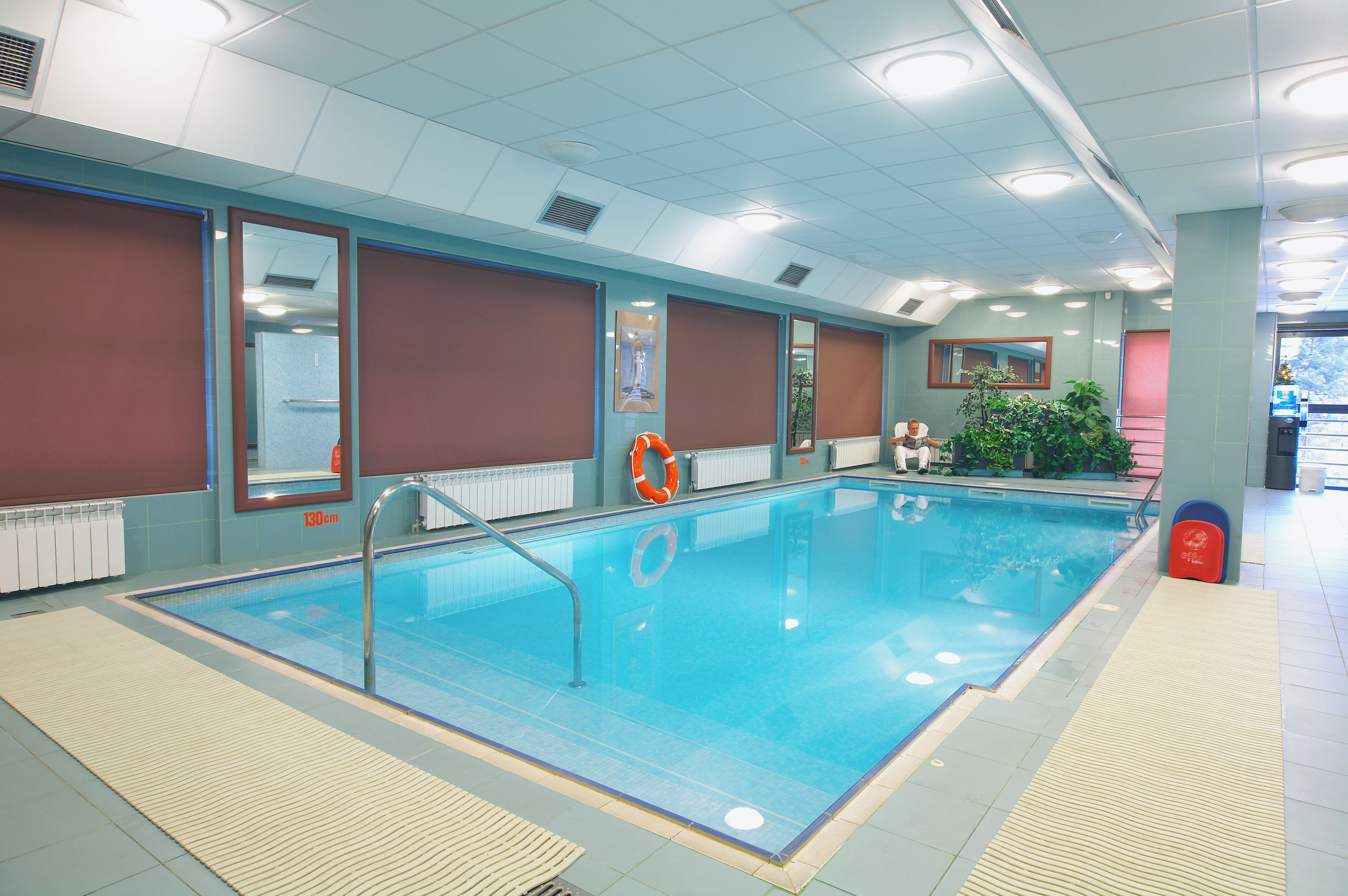 An indoor swimming pool with clear water, safety equipment, and a tiled floor.