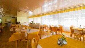A dining area with multiple tables and chairs, large windows with sheer curtains, and a kitchen area in the background. - Geovita Krynica Zdroj (Krynica-Zdroj)