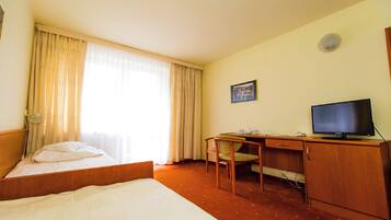 A hotel room with a bed, a desk with a chair, a television, and a window with curtains.