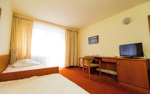A hotel room with a bed, a desk with a chair, a television, and a window with curtains. - Geovita Krynica Zdroj (Krynica-Zdroj)