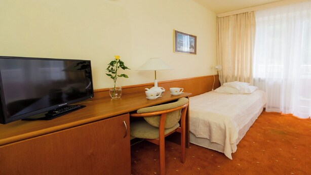 A hotel room with a television, a desk with a lamp, a chair, a bed, and a window with curtains. - Geovita Krynica Zdroj (Krynica-Zdroj)