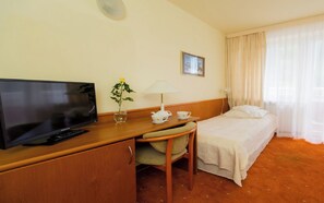 A hotel room with a television, a desk with a lamp, a chair, a bed, and a window with curtains. - Geovita Krynica Zdroj (Krynica-Zdroj)