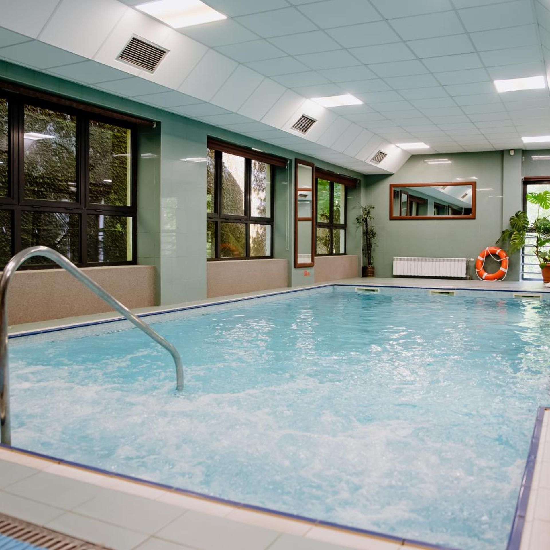 An indoor swimming pool with clear water, a metal ladder, and a lifebuoy.