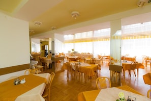 Un vaste espace dédié à la salle à manger, avec de nombreuses tables et chaises, de grandes fenêtres dotées de rideaux et un intérieur lumineux.