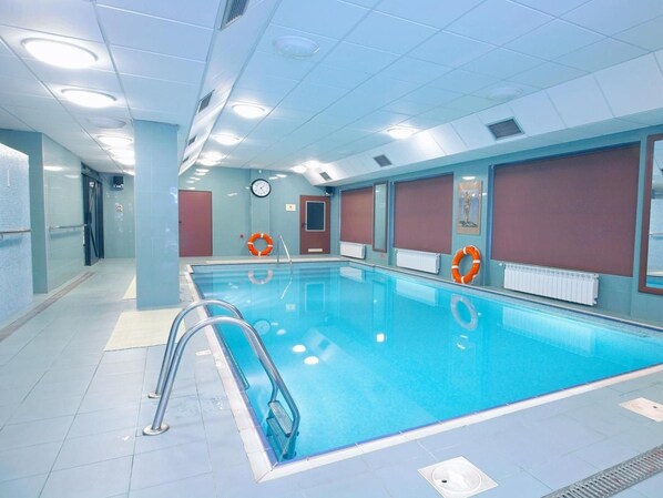An indoor swimming pool with clear water, surrounded by walls with windows and doors, and equipped with safety equipment. - Geovita Krynica Zdroj (Krynica-Zdroj)