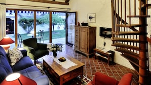 A spacious living room with a high ceiling, wooden beams, a spiral staircase, and a large window offering a view of the outdoors. - Herberge an der Nikolauszeche (Purbach am Neusiedlersee)