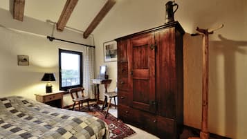 A bedroom with a large bed, wooden wardrobe, and a desk with a lamp.