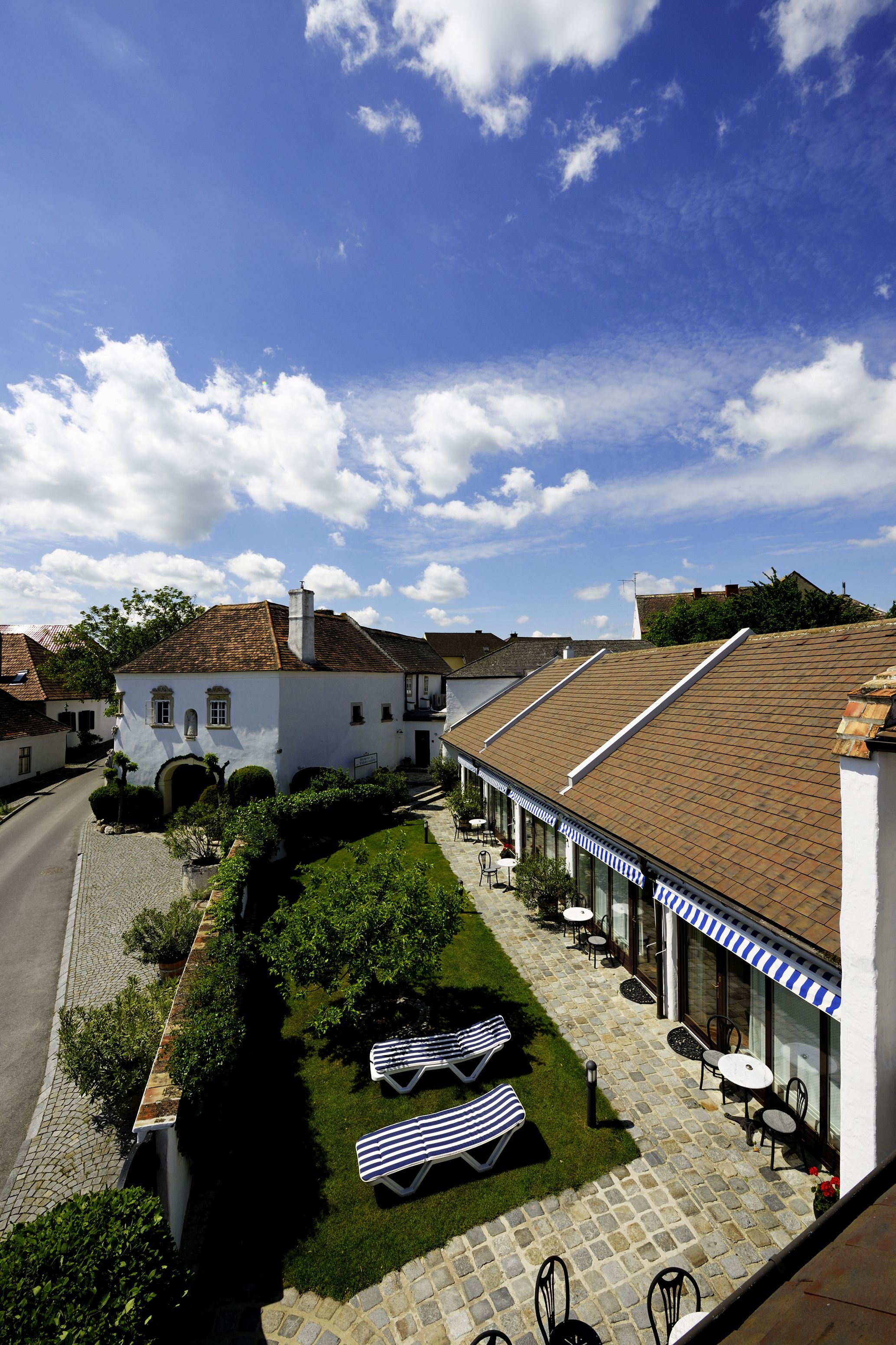 Une cour avec un bâtiment blanc, un chemin pavé et des sièges extérieurs.