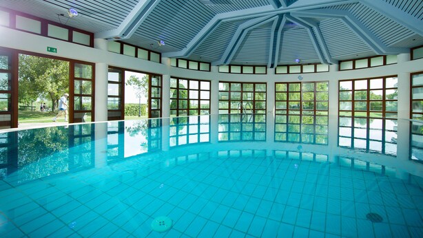 An indoor swimming pool with a high ceiling and large windows. - Seehotel Rust (Rust)