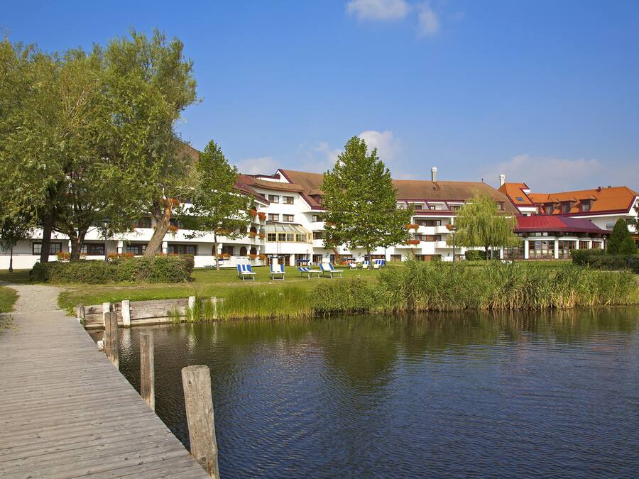 Un hotel frente al lago con un muelle de madera, sillas de descanso y vistas al agua.