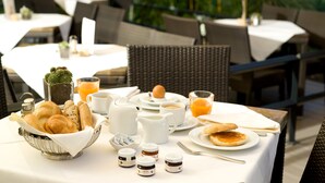 A breakfast setting with a variety of food items, including pastries, eggs, and juice, on an outdoor table with wicker chairs and a white tablecloth. - Seehotel Rust (Rust)