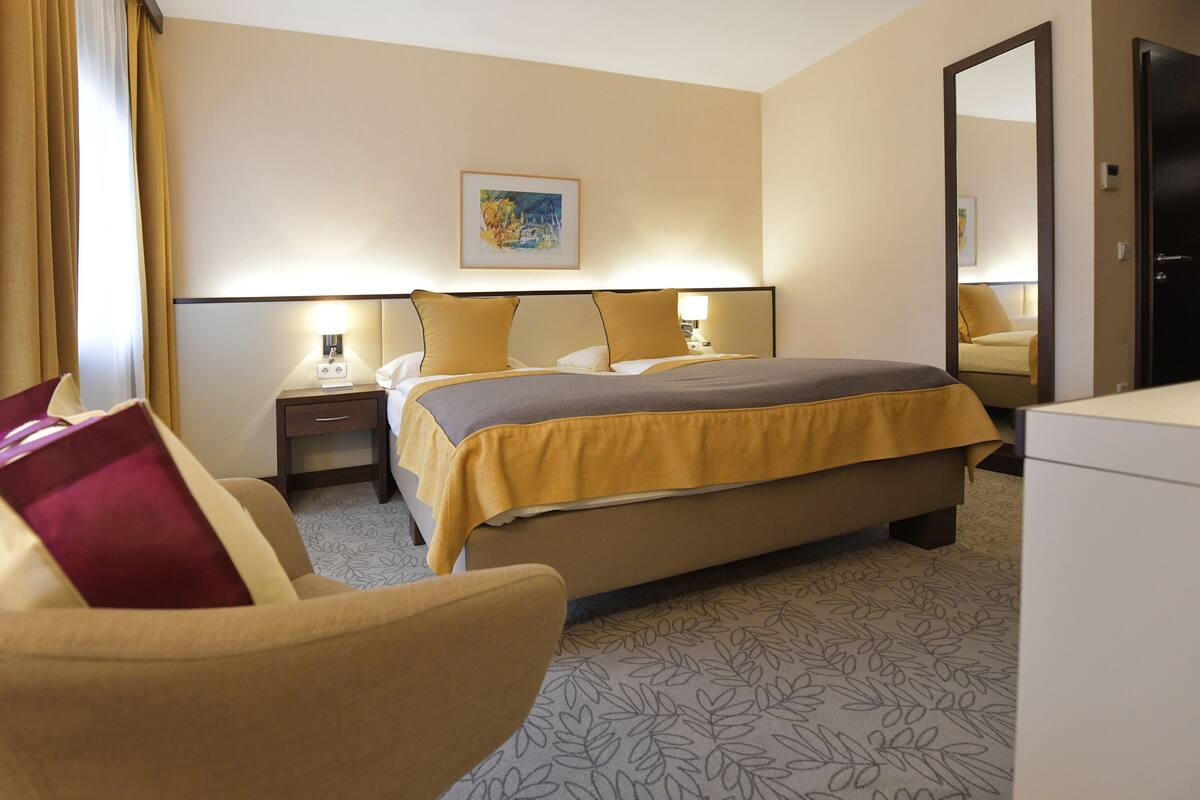 Habitación de hotel con cama, mesitas de noche, escritorio, silla, espejo y un cuadro en la pared.