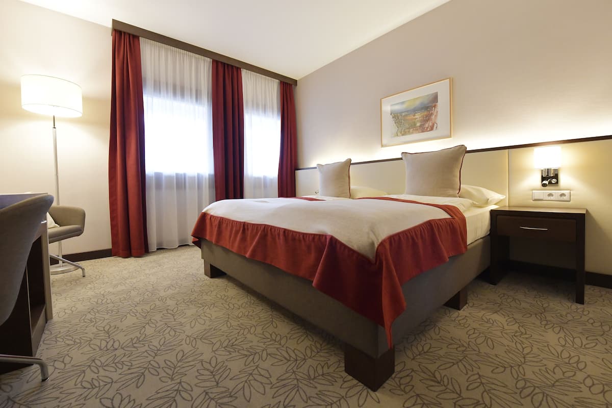 Una habitación de hotel con una cama grande, un escritorio, una silla, una mesita de noche y una lámpara.