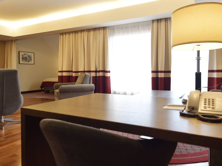 A hotel room with a desk, a chair, a bed, a lamp, and a telephone.