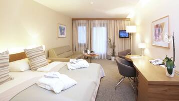 Ein Hotelzimmer mit Bett, Schreibtisch, Stuhl, Fernseher und einem Fenster mit Vorhängen.