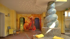 A lobby with a spiral stone sculpture, a large mural, and a reception desk. - Seehotel Rust (Rust)