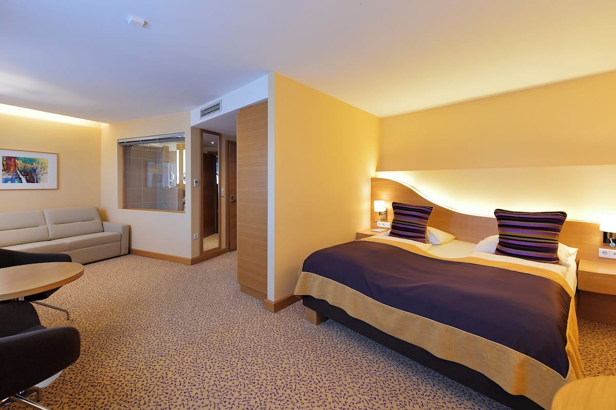 Una habitación de hotel con cama, sofá, mesa de comedor y una pequeña cocina.