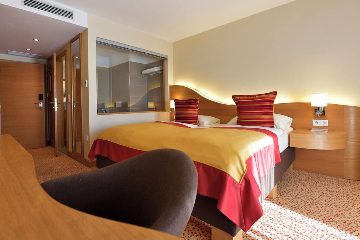 Habitación de hotel con cama, escritorio, silla, espejo y mesita de noche con lámpara.