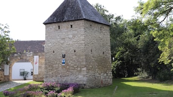 Una torre in pietra con tetto a cono, circondata da un giardino curato con fiori viola.