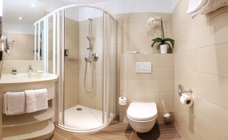 Un baño moderno con ducha de vidrio, inodoro y lavamanos con toallero.