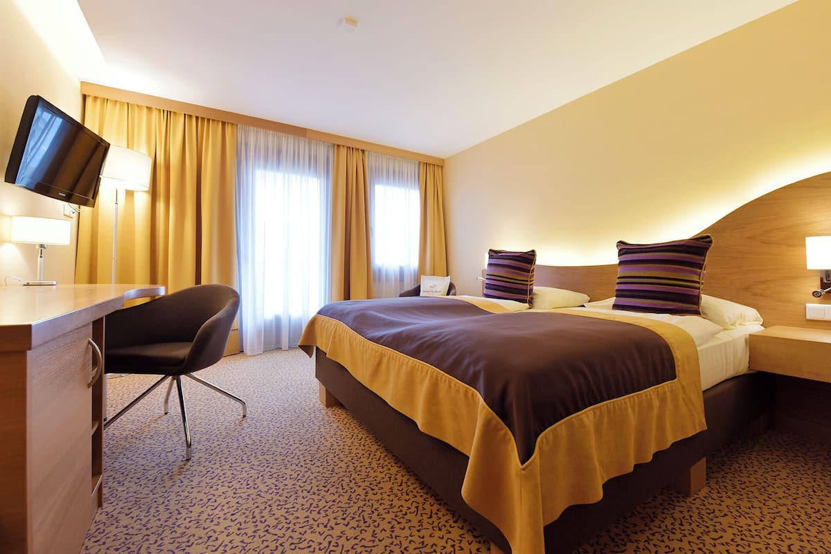 Habitación de hotel con una cama grande, un escritorio con ordenador, una silla y un televisor.