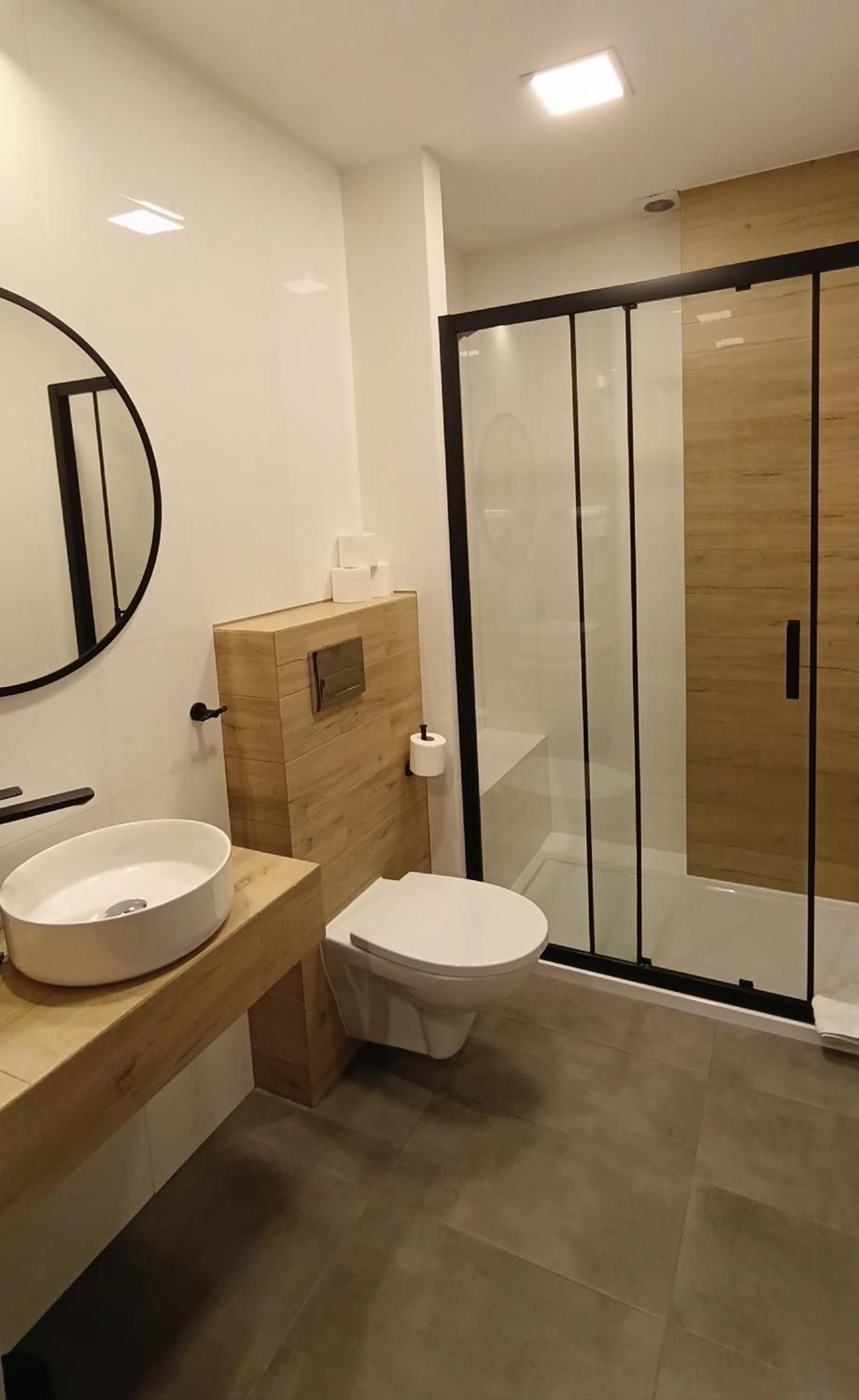 Une salle de bain moderne avec un miroir rond, des toilettes et un espace douche.