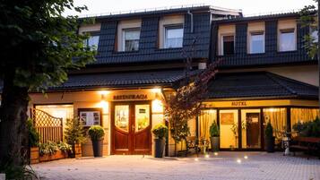 A hotel with a restaurant on the ground floor, featuring a traditional facade, a wooden entrance, and a paved courtyard.