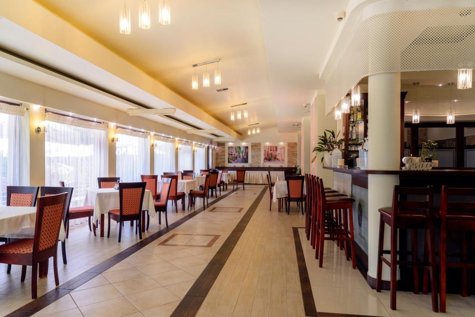 Un comedor de hotel con varias mesas y sillas, una barra y un largo pasillo con ventanas.