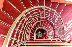 Un escalier en colimaçon avec un mur recouvert d’une moquette rouge et une rampe en métal.