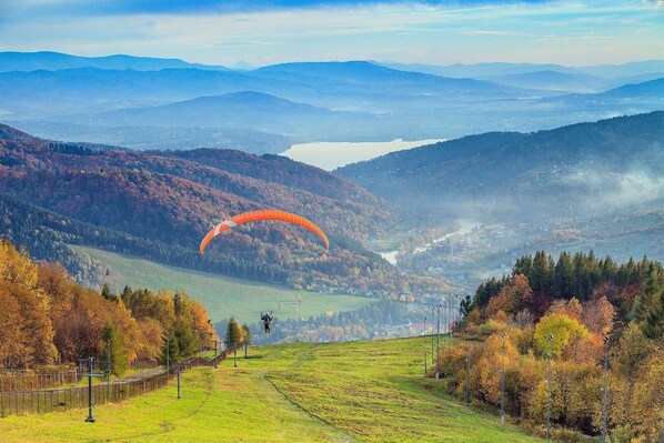 Un paysage montagneux où l’on voit une personne faire du parapente au-dessus d’une vallée.