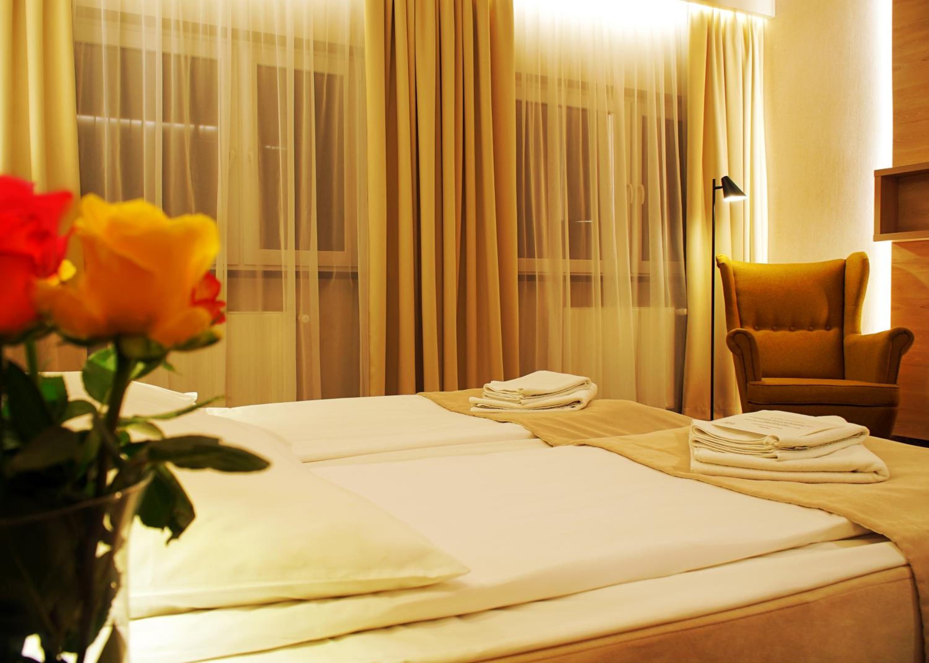 A hotel room with a bed, a chair, a lamp, and a vase with flowers.