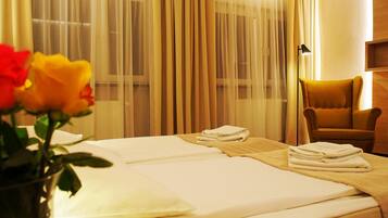 A hotel room with a bed, a chair, a lamp, and a vase with flowers.