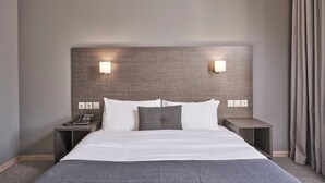 A hotel room with a large bed, two bedside tables, a telephone, and wall-mounted lights.