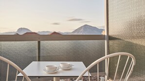 A balcony with a table and two chairs, overlooking a mountainous landscape.
